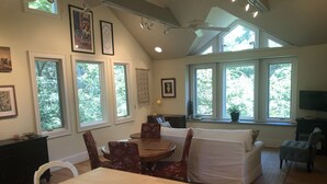 A spacious living room with a high ceiling, large windows, a dining area, and a cozy seating area.