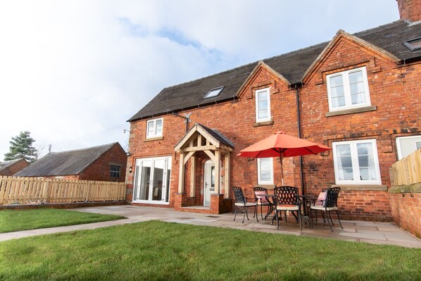 A brick house with a patio, a wooden fence, and a red umbrella.