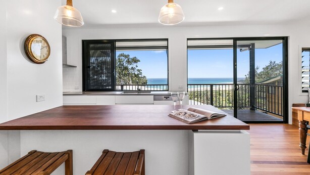 A modern kitchen with a large island, wooden stools, and a view of the ocean through large windows. - Beautiful Apartment built 2019 (Point Lookout)