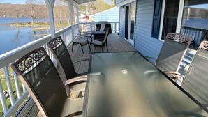 A covered deck with a table and chairs, overlooking a lake. - Relaxing Lake House - Enjoy the Sun and Fun!!! (Erieville)