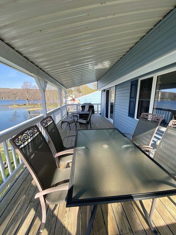 A covered deck with a table and chairs, overlooking a lake. - Relaxing Lake House - Enjoy the Sun and Fun!!! (Erieville)