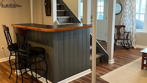 A kitchen with a bar area, wooden flooring, and a staircase leading to another room. - Relaxing Lake House - Enjoy the Sun and Fun!!! (Erieville)