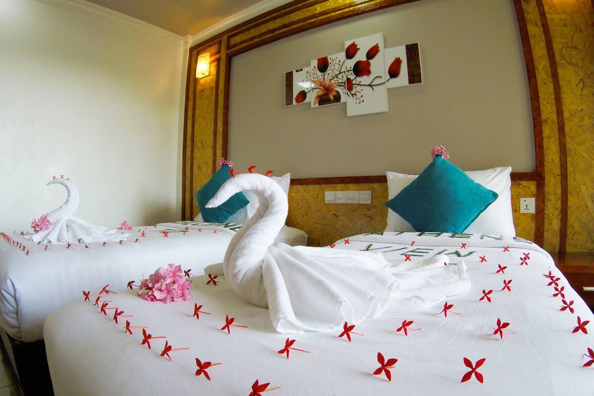 A hotel room with two beds, each adorned with swan-shaped towels and red floral patterns.