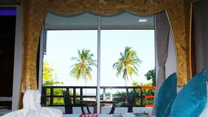 Una habitación de hotel con un gran ventanal, una cama con ropa blanca y vistas a palmeras.