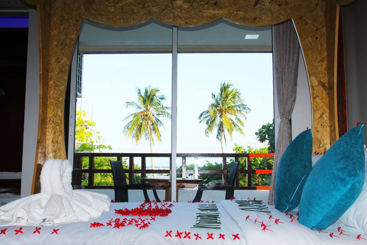 A hotel room with a large window, a bed with white linens, and a view of palm trees.