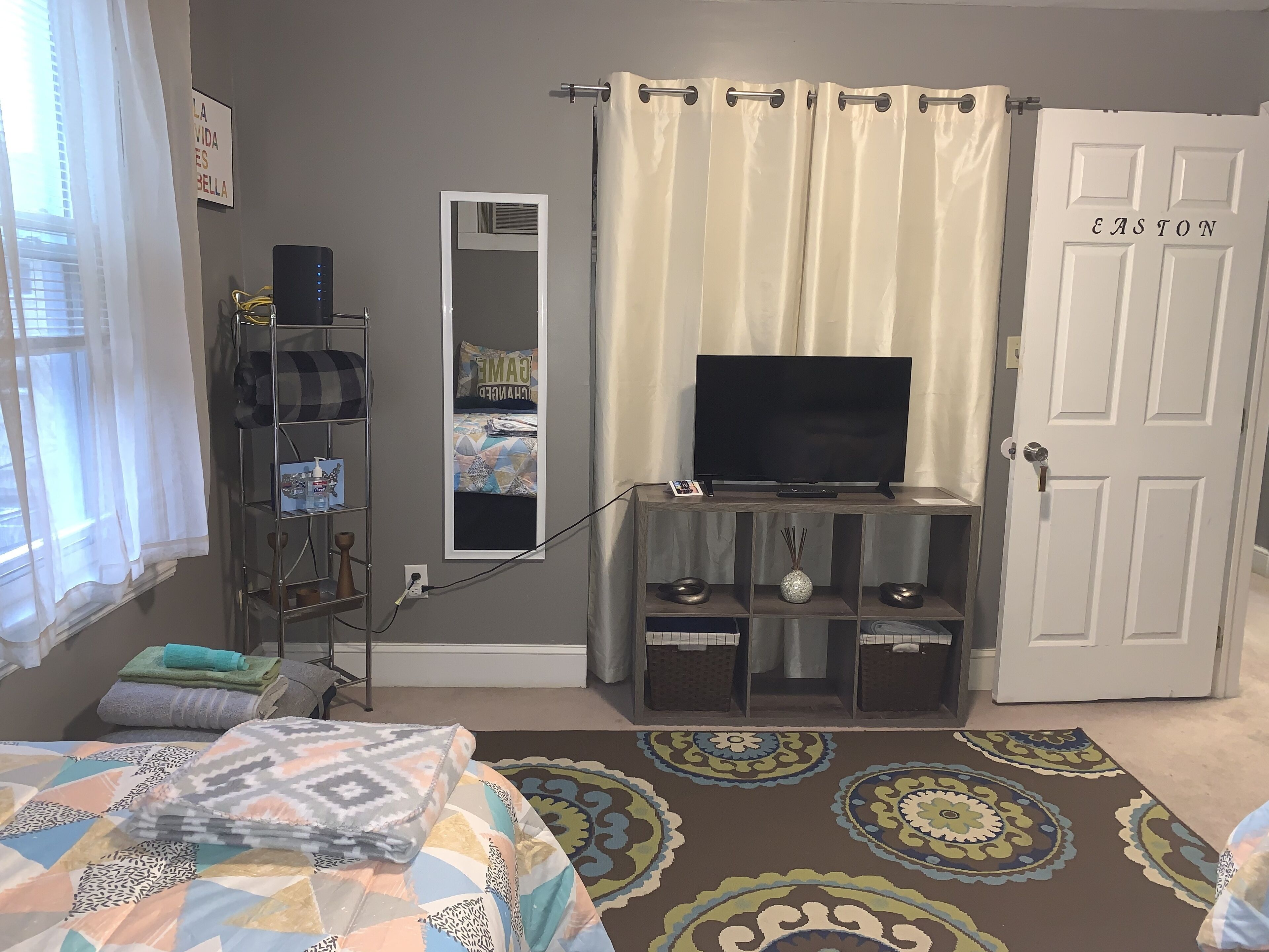 A bedroom with a bed, a TV, a wardrobe, a mirror, and a door.