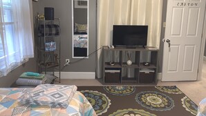 Une chambre à coucher avec un lit, un téléviseur posé sur un meuble, une armoire, un miroir et une porte.