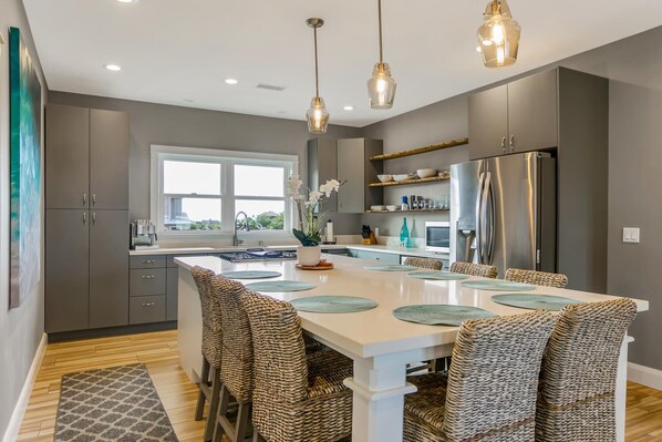 A modern kitchen with a central island, stainless steel appliances, and woven chairs.