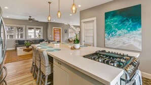 Et moderne køkken med en central ø, hængende lamper og et stort maleri med havtema.
