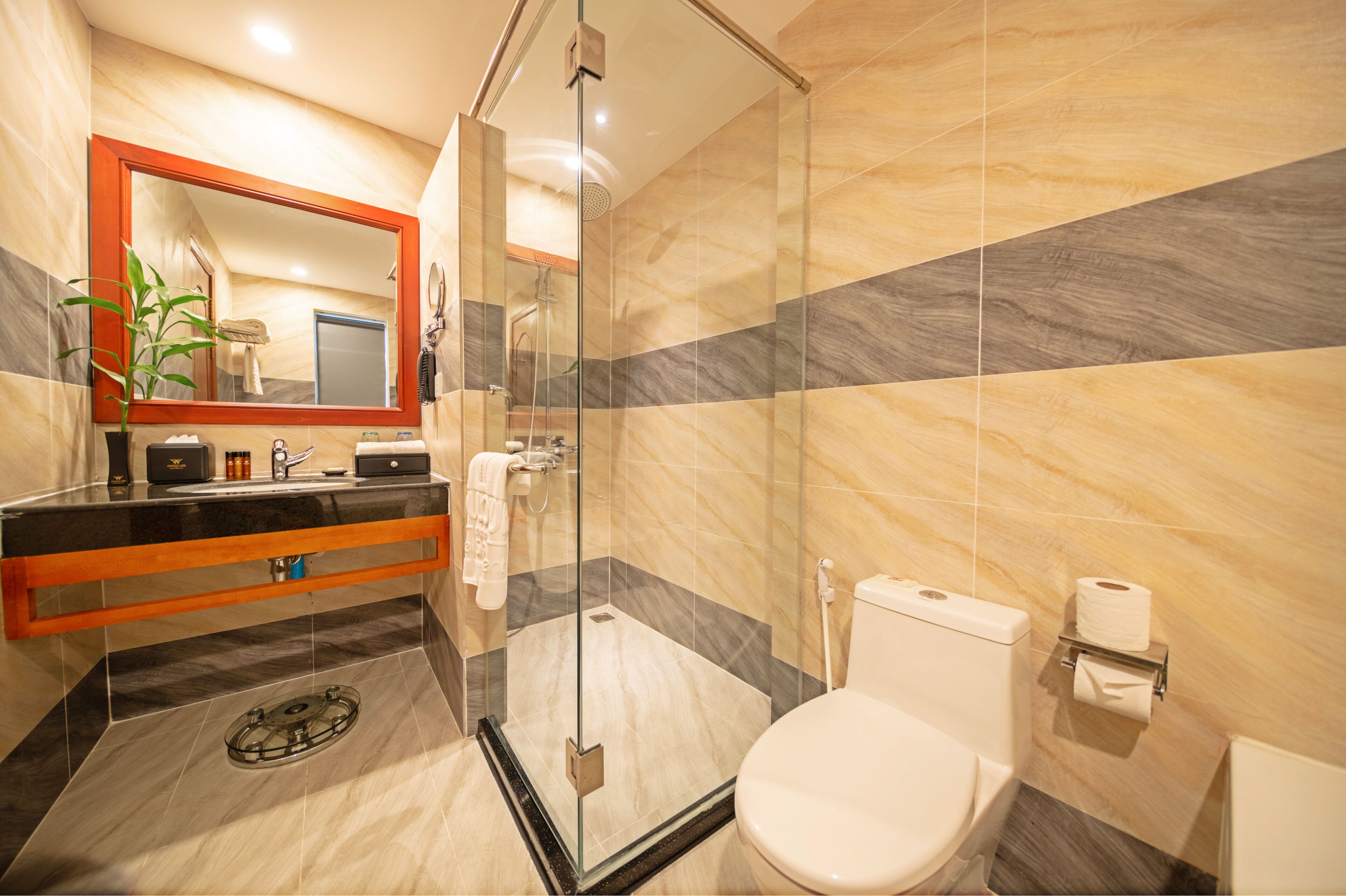 A modern bathroom with a glass-enclosed shower, a marble-tiled floor, a black countertop, and a white toilet.