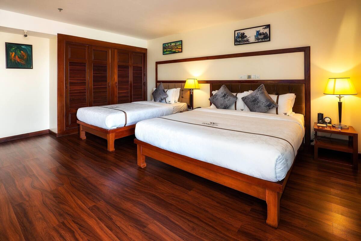 Habitación de hotel con dos camas, suelo de madera y cabecero de madera.