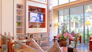 Un moderno hall de hotel con un televisor grande en la pared, asientos cómodos y vistas al exterior a través de amplias ventanas.