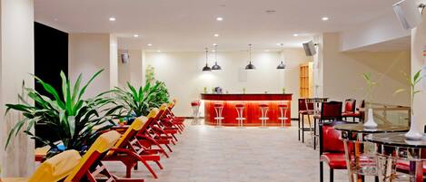 A spacious hotel lobby with a long reception desk, multiple seating areas, and potted plants.