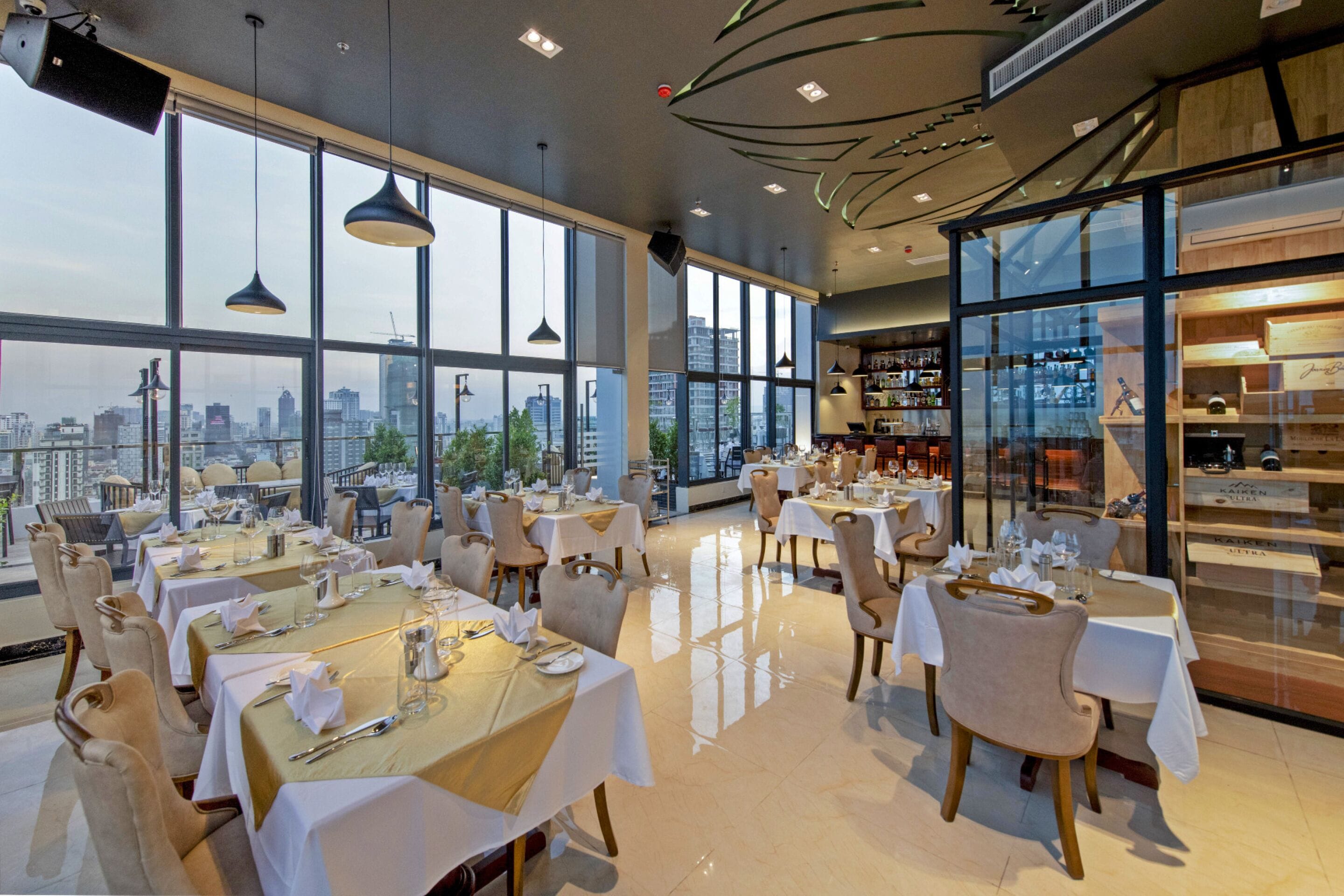 A restaurant with tables set for dining, large windows offering a city view, and a modern interior design.