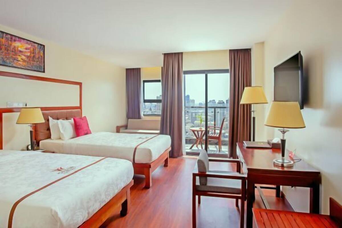Habitación de hotel con dos camas, un escritorio, una silla, un televisor y vistas a la ciudad.