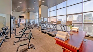 Un gimnasio con cintas de correr, máquinas de pesas y un amplio ventanal con vistas a la ciudad.