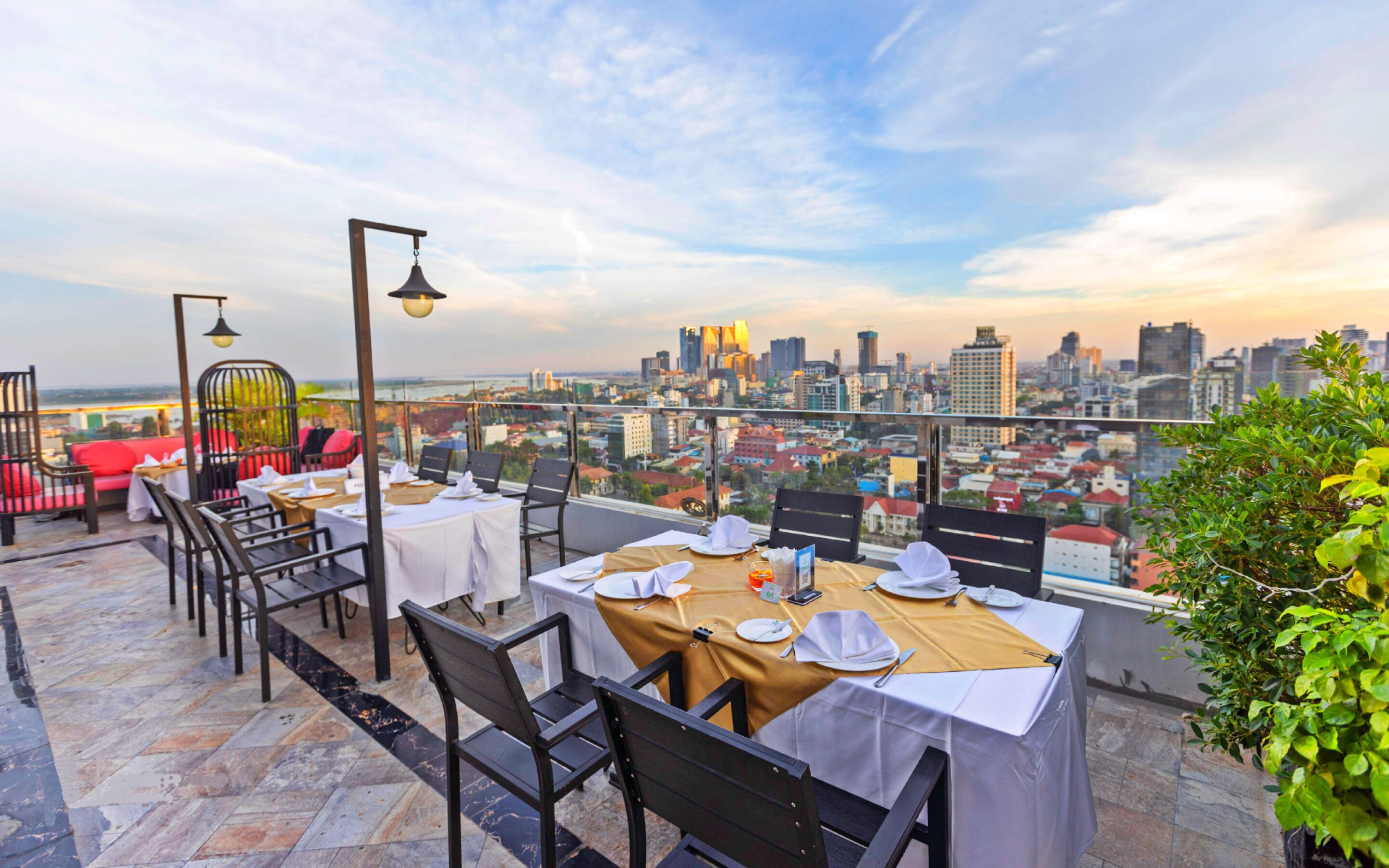 A rooftop restaurant with tables set for dining, overlooking a cityscape.