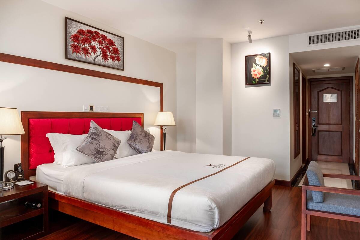 Una habitación de hotel con una cama grande, dos mesitas de noche, una silla y obras de arte en las paredes.