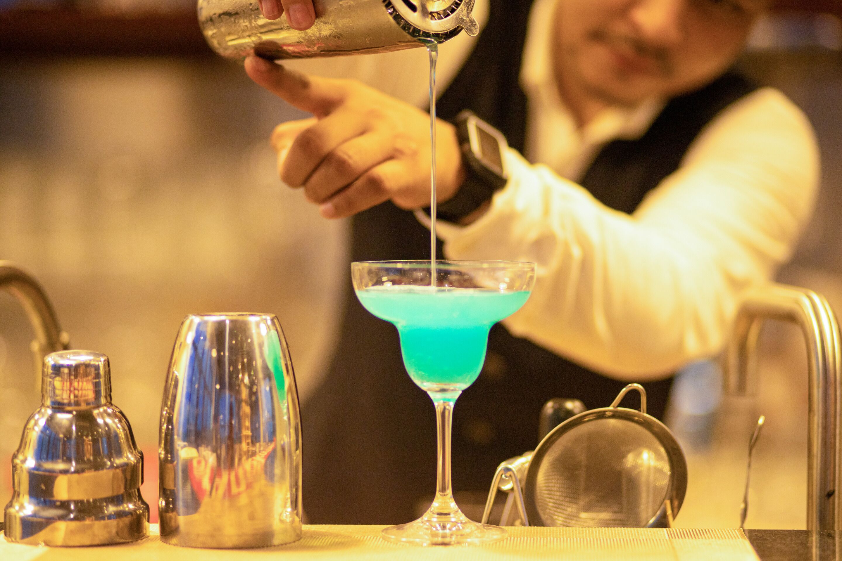 A bartender pouring a blue liquid into a martini glass.