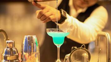 A bartender pouring a blue liquid into a martini glass.