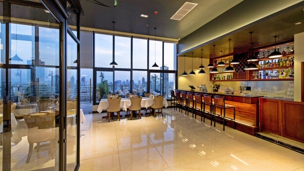 Un bar de hotel moderno con amplios ventanales, vistas a la ciudad y un interior elegante.