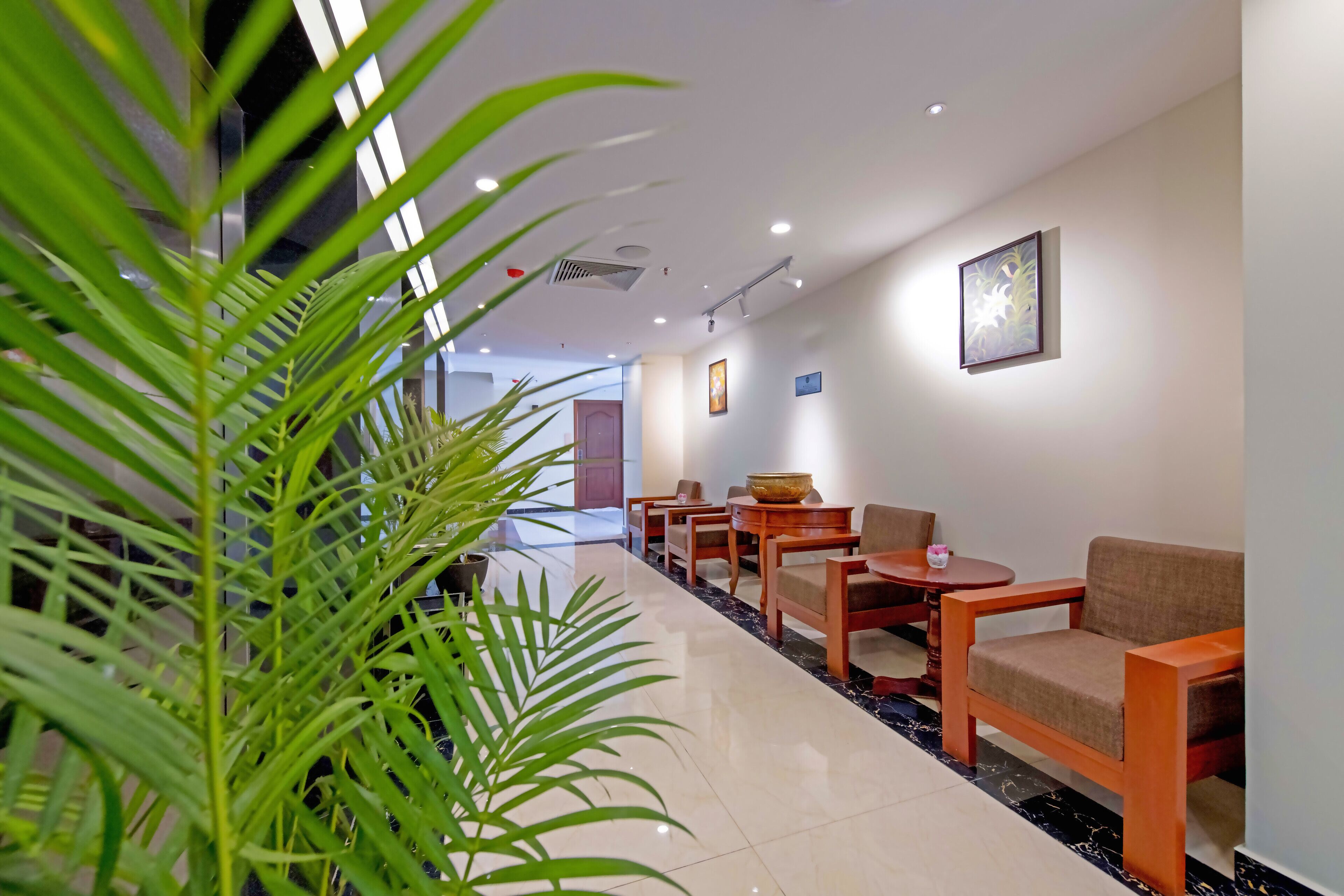 Een hotel lobby met een lange receptiebalie, verschillende zithoeken en een grote kamerplant.