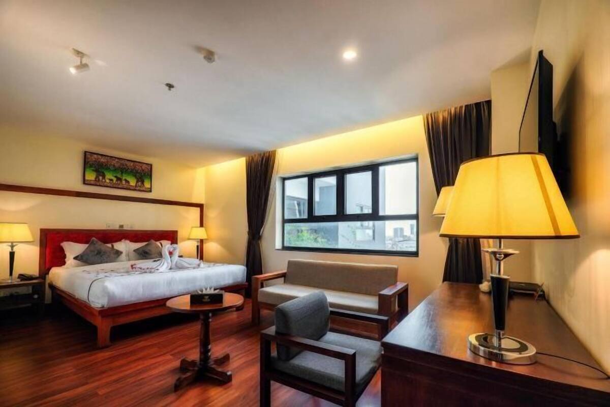 Una habitación de hotel con cama, sofá, escritorio, lámpara y ventana.
