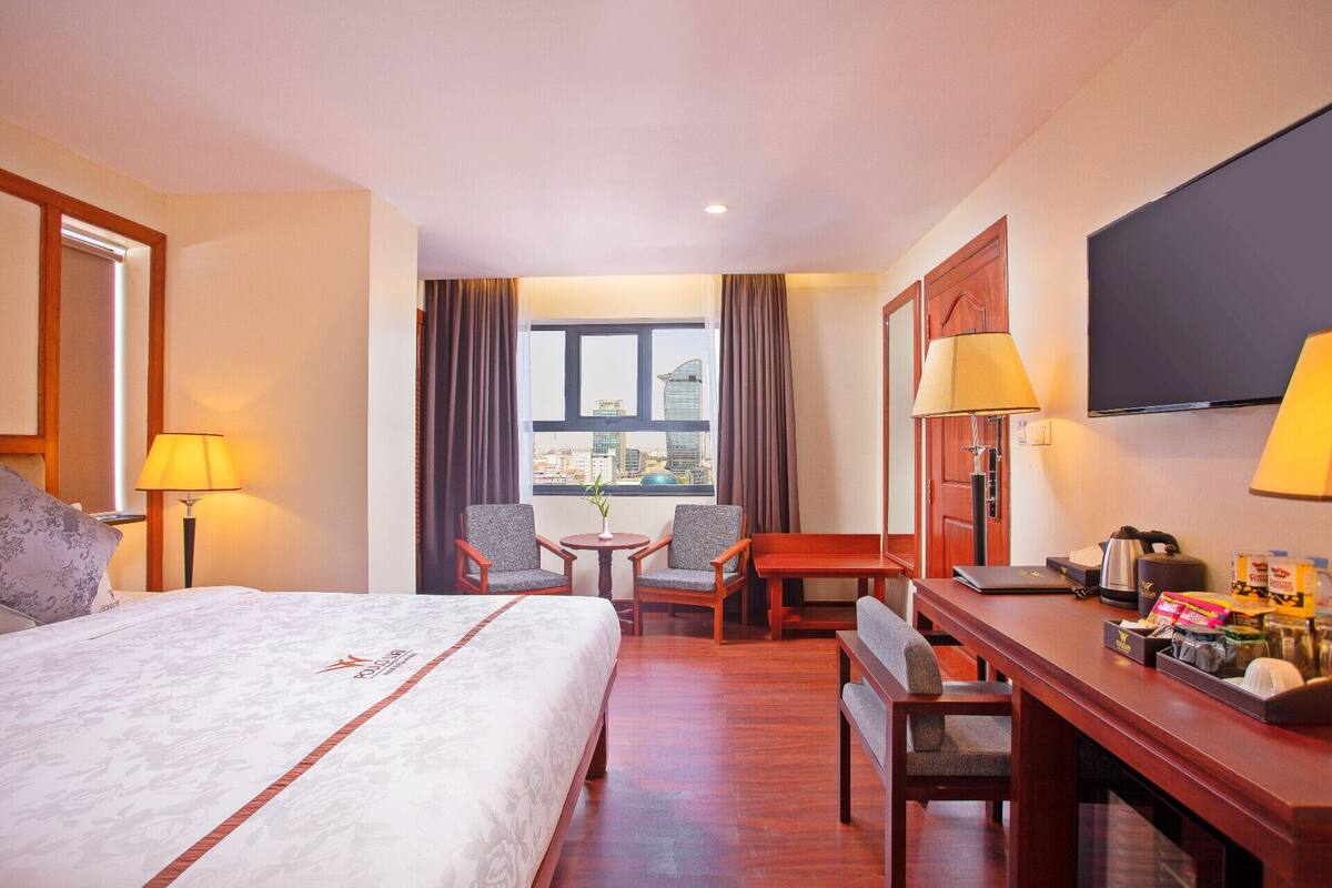 Habitación de hotel con cama, dos sillones, una mesita, un escritorio con computadora y televisor.