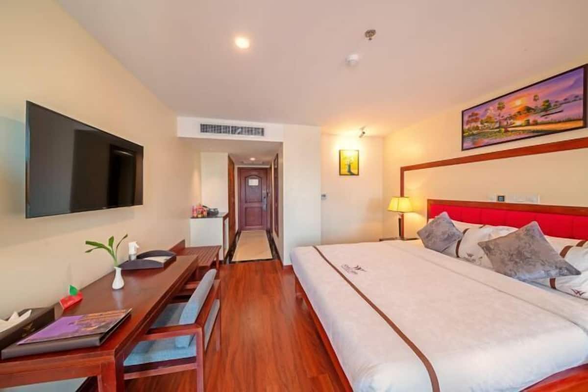 Habitación de hotel con cama, escritorio, televisor de pantalla plana, un cuadro y un pasillo.