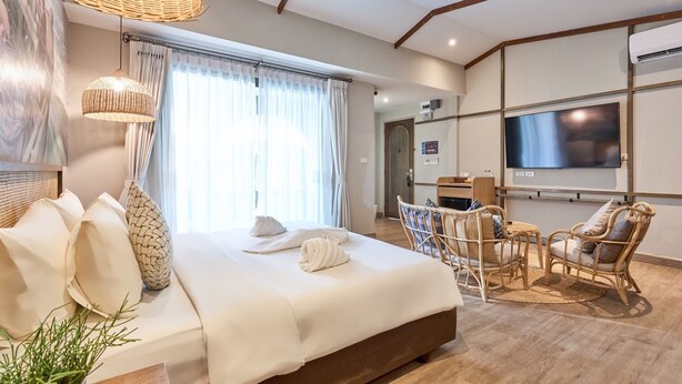 A hotel room with a bed, a TV, wicker furniture, and a large window with curtains. - Barabara Budget Satun (La-ngu)