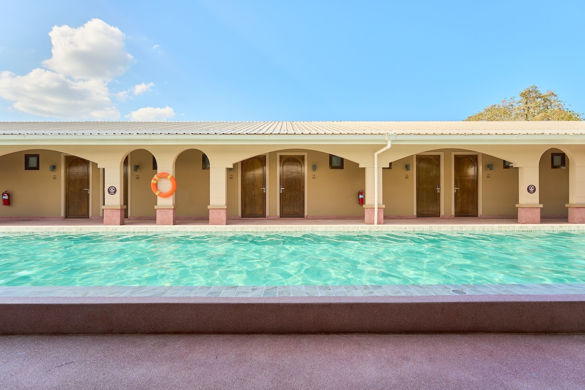 A hotel with a swimming pool, multiple doors, and a covered walkway.