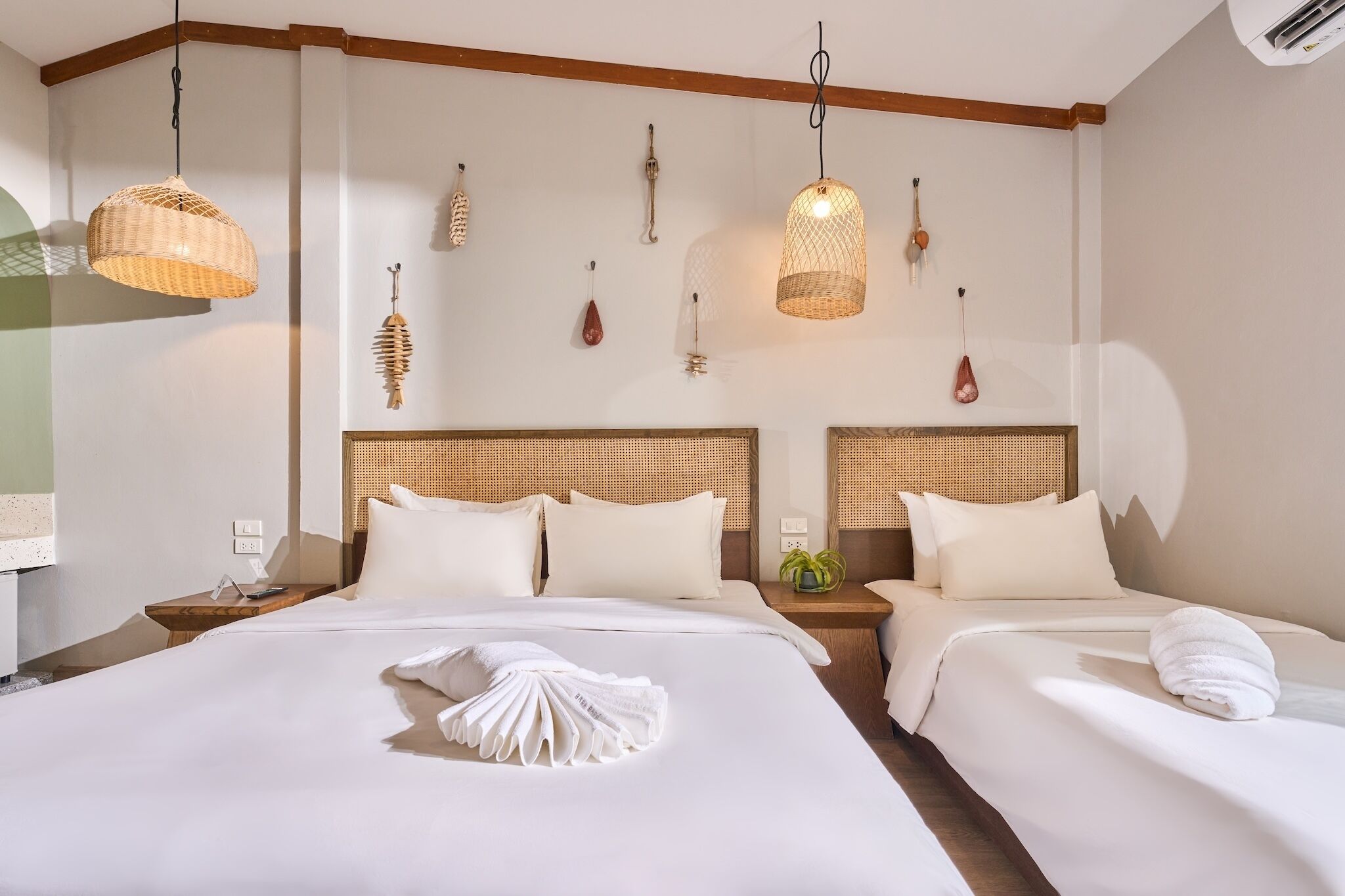 Ein Hotelzimmer mit zwei Betten, einem Holzkopfteil, einer Hängelampe und einer kleinen Pflanze auf dem Nachttisch.