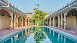 A swimming pool with a reflection, surrounded by arched walkways and a building with a tower in the background. - Barabara Budget Satun (La-ngu)