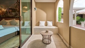 A room with a bed, a glass partition, a round wicker table, and a bench with pillows. - Barabara Budget Satun (La-ngu)
