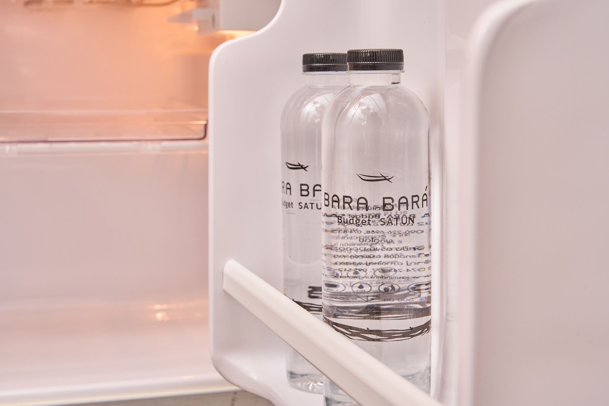 A refrigerator with two bottles labeled 'BARÁ SATUSTRIÑE' and 'Budget SATUSTRIÑE' inside.