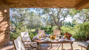 An outdoor dining area with a wooden table set for four, surrounded by chairs, with a view of trees and greenery. - Cala Sultana by Interhome (Porto Vecchio)