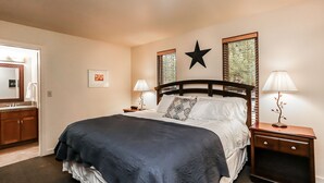 A neatly arranged bedroom with a large bed, two bedside tables with lamps, a star decoration on the wall, and a window with blinds. - Stunning Views, Closest to Mt. Bachelor, Resort Amenities & Year-Round Fun! (Bend)