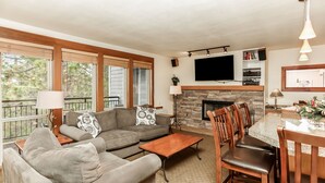 A living room with a fireplace, a television mounted above it, and a dining area with a table and chairs. - Stunning Views, Closest to Mt. Bachelor, Resort Amenities & Year-Round Fun! (Bend)