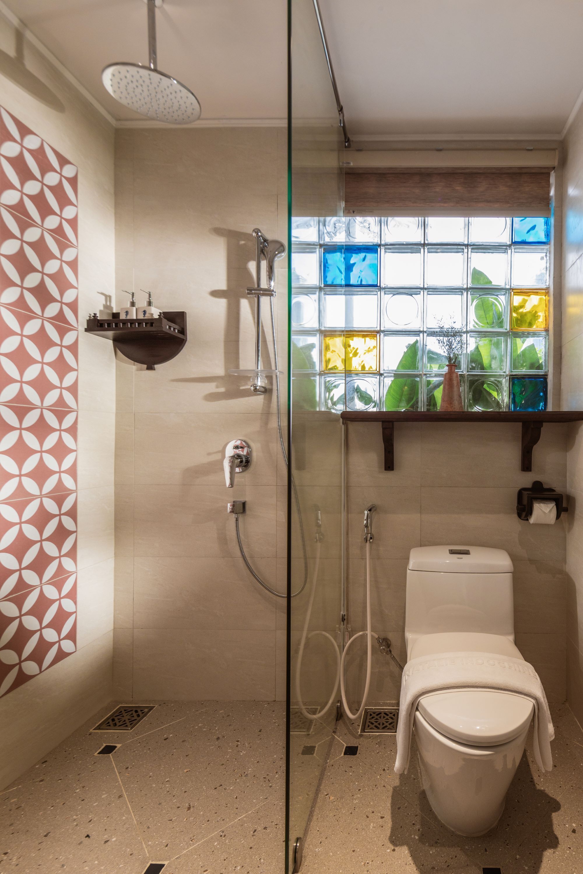 A modern bathroom with a glass shower enclosure, a white toilet, and a window with colorful glass panes.