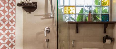 A modern bathroom with a glass shower enclosure, a white toilet, and a window with colorful glass panes.