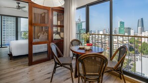 A modern hotel room with a balcony, wooden flooring, wicker chairs, a round dining table, and a city view. - Seahorse Tropical Natalie Da Nang Hotel by Haviland (Da Nang)