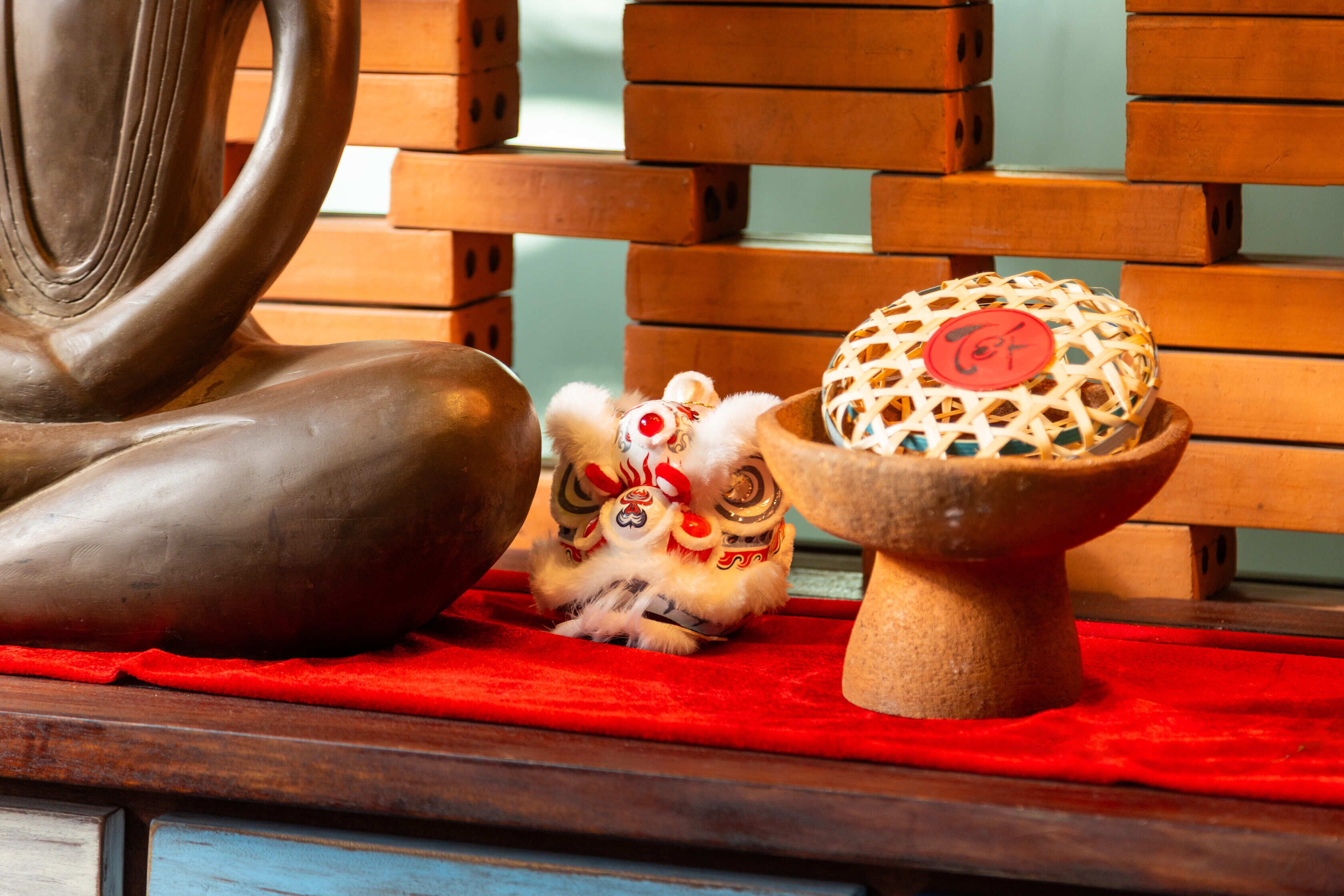 A traditional Chinese lion dance figure on a red cloth, a wooden sculpture, and a woven basket with a red lid.
