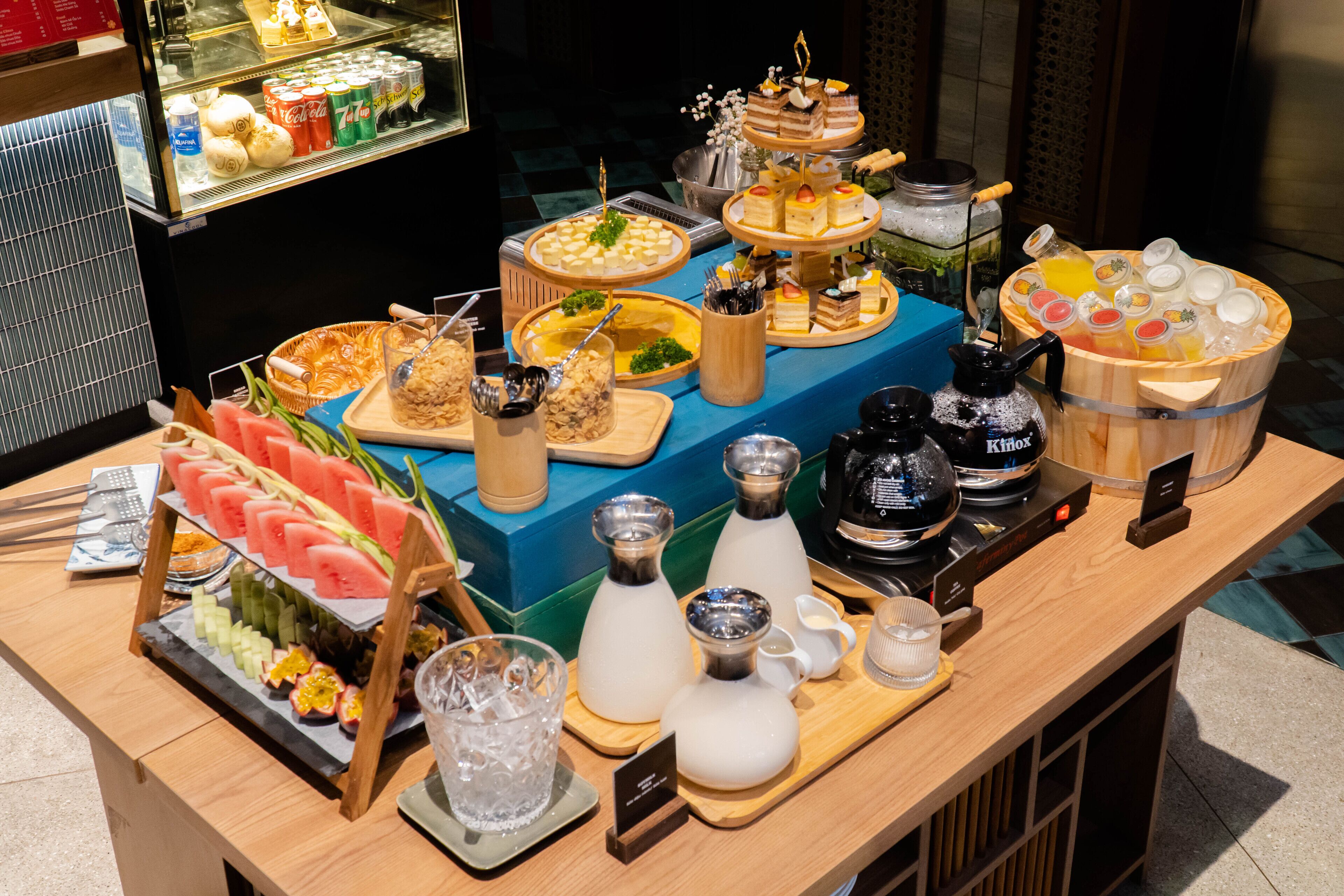 A buffet with various food items and beverages, including fruits, desserts, and a coffee station.