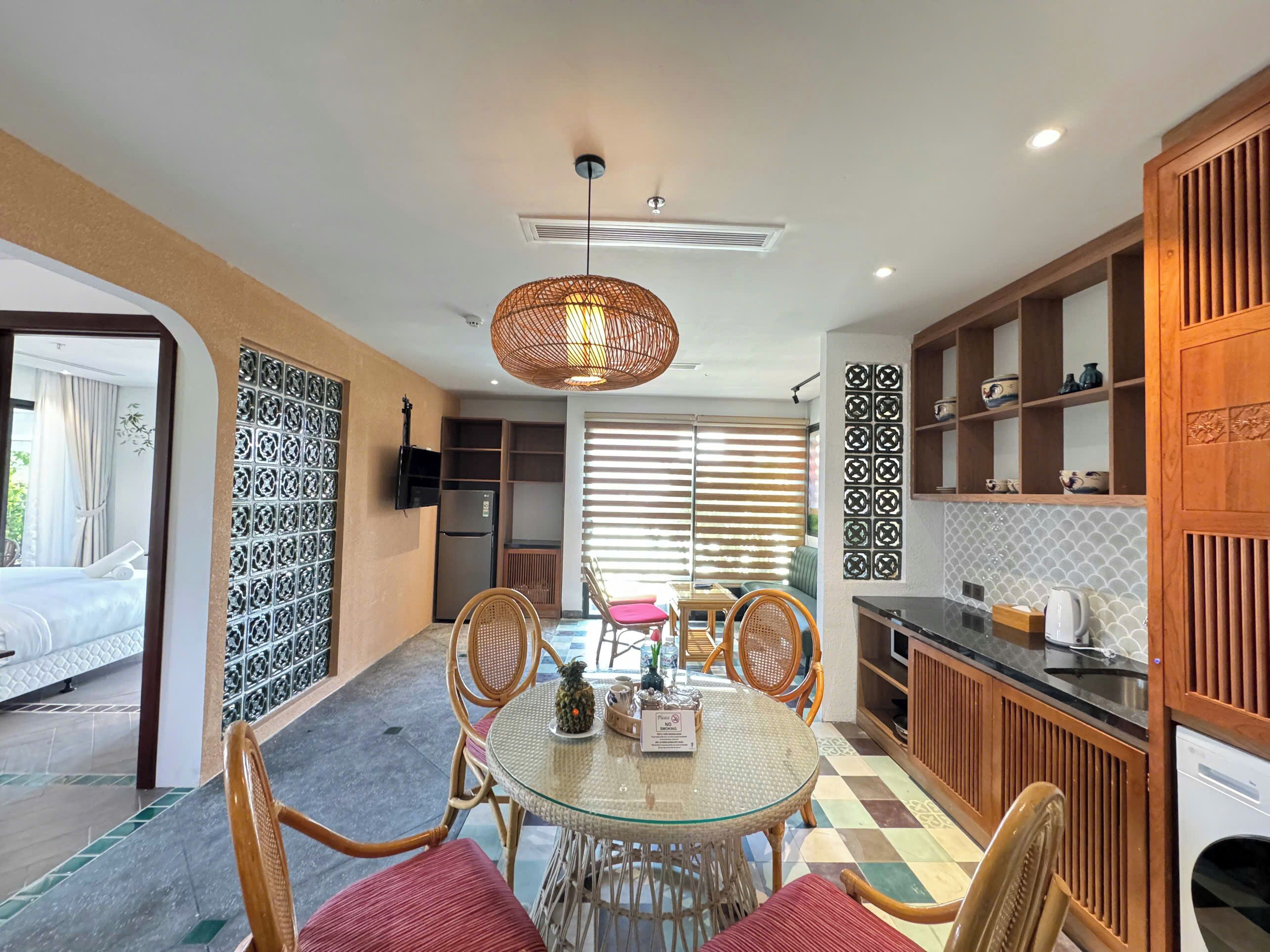 A modern kitchen with a dining area, featuring a round glass table, wicker chairs, and a hanging light fixture.