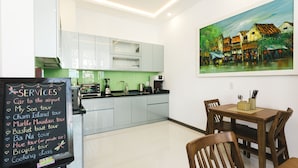 A modern kitchen with light blue cabinets, a dining table with chairs, and a painting on the wall. - Le Petit Villa Hoi An (Da Nang)
