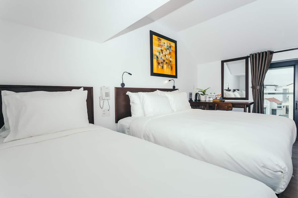 A hotel room with two beds, a desk with a telephone, a mirror, and a window with curtains.