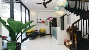 A modern living room with a large potted plant, a ceiling fan, and a staircase with a black railing. - Le Petit Villa Hoi An (Da Nang)
