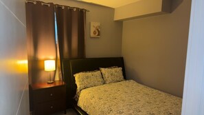 A bedroom with a bed, a nightstand, a lamp, and a wall-mounted picture.