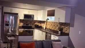 A modern kitchen with stainless steel appliances, a microwave, and a built-in oven. There is a bar stool and a seating area with a couch.