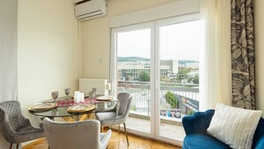 Ein Essbereich mit einem für vier Personen gedeckten Tisch, einem blauen Sofa und Blick auf eine Stadtlandschaft durch große Fenster.